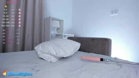 Media: Video of a minimalist bedroom with a white bed, gray headboard, white pillows, beige curtains, and a white nightstand with a lamp. A pink vibrator lies on the bed.