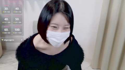 Media: Video of an Asian woman with short black hair, wearing a white face mask, black fur-trimmed top, and a white background, with a digital overlay of health stats.