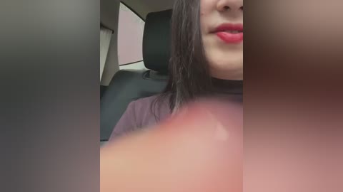 Media: A video of a woman with long black hair, fair skin, and red lipstick, partially visible from the neck down, seated in a car with black leather seats.