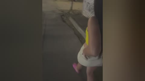 Media: A video shows a person wearing a striped shirt and white shorts, with a pink shoe, standing in a dimly lit, narrow alleyway with a concrete wall and curb.