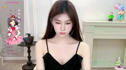 Media: A video of an East Asian woman with long black hair, wearing a black dress, sitting in a room with a calendar, toys, and a fireplace in the background.