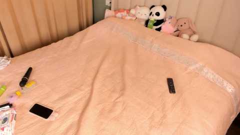 Media: Video of a bed with a beige duvet, featuring stuffed animals and a smartphone on the left, a wallet on the right, and a black pen.