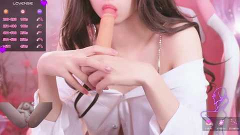 Media: Video of an Asian woman with long brown hair, wearing an off-shoulder white top, performing oral sex with a large, realistic-looking dildo. Pink background with a social media user interface on the left.