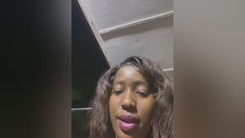 Media: Video of a Black woman with curly, shoulder-length brown hair, wearing dark lipstick, captured from a low angle, indoors under fluorescent lighting.