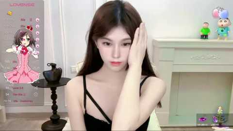 Media: A video of a young Asian woman with long brown hair, wearing a black dress, sitting on the floor, looking sad. Background includes a white fireplace, a small table, and colorful toy figures.