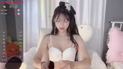 Media: A video of an Asian woman with long black hair and a white bra, sitting on a plush bed with a plush toy, wearing a white headband.