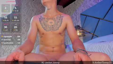 Media: Video of a nude, fit, light-skinned man with tattoos on his chest, sitting on a bed in a dimly lit, modern room. Digital overlay shows \"IG Amber Tunny\" and \"XamberTunny25\" usernames.