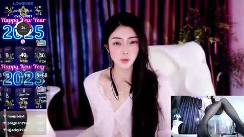 Media: A video of an Asian woman with long black hair, wearing a white sweater, sitting in a modern living room with a \"2023\" and \"Happy New Year\" digital display.