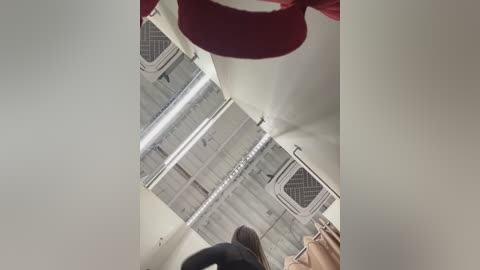 Media: Video of a person wearing a red and white sweater, standing in a dimly lit, narrow corridor with exposed ceiling ducts and a beige floor.