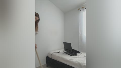 Media: A video of a minimalist, empty bedroom with white walls, a single bed with white sheets, a laptop on the floor, and a partially visible person peering from behind a corner.