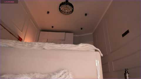 Media: A video of a minimalist, white-walled room with a bed, white curtains, and a crystal chandelier. The room is dimly lit, creating a serene ambiance.