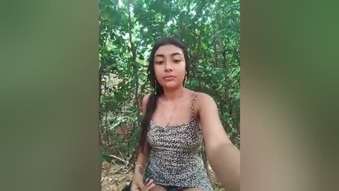 Media: Video of a Latina woman with long, dark hair, wearing a leopard-print dress, sitting in a lush, green forest.