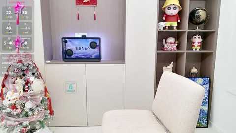 Media: Video of a modern, minimalist living room with a white couch, a TV on a white cabinet, a Christmas tree adorned with red and white ornaments, and a wooden bookshelf with toys and books.