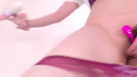 Media: Video of a woman with fair skin, wearing lacy maroon lingerie, using a pink vibrator on her stomach. Background is soft focus, possibly a bathroom.