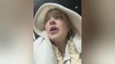 Media: Video of a blonde woman in a white hooded cloak with braided hair, looking shocked or startled, with blurred background.