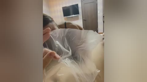 Media: Video of a person wearing a clear plastic bag over their head, with a blurred background featuring a TV and wooden door.