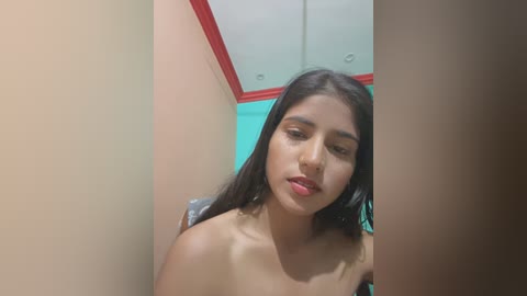 Media: A video shows a young, dark-haired woman with olive skin, wearing red lipstick, standing topless in a bathroom with a teal wall and red trim.