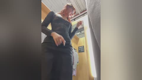 Media: Video of a woman in a dressing room with a yellow curtain, adjusting a black lace bodysuit. She has shoulder-length auburn hair, and the room has a metal ceiling.