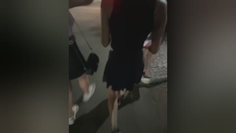 Media: A blurred video shows a woman in a black dress walking away, holding a black handbag. The background includes a grey floor and dim lighting.