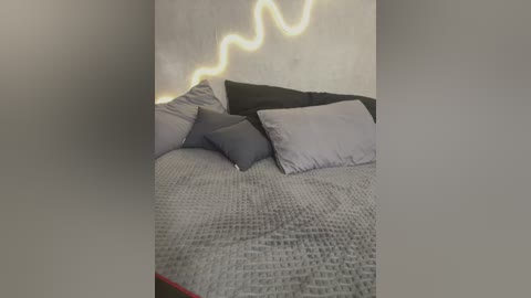 Media: Video of a modern bedroom with a gray textured blanket, black and gray pillows, and a wall-mounted light strip mimicking a lightning bolt, creating a striking contrast against the beige wall.