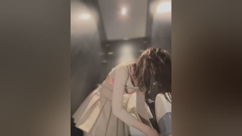 Media: A video depicts a woman with wavy brown hair in a beige dress, leaning over a man in a gray shirt, both seated in a dimly lit, narrow, subway-like corridor.