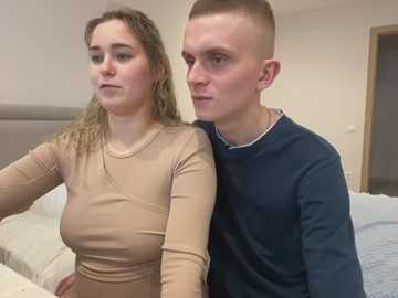 Media: A video of a couple sitting on a bed, a woman with shoulder-length blonde hair in a beige top, and a man with a shaved head in a navy blue sweater, both looking serious.