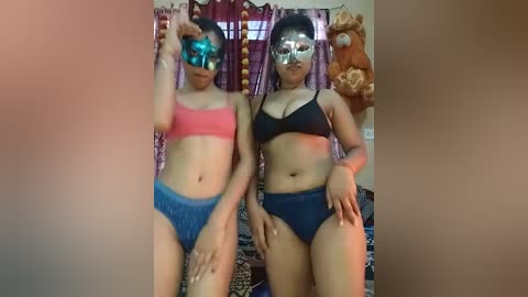 Media: A video of two women wearing bikinis and reflective sunglasses, standing side by side in a dimly lit room with purple curtains and stuffed animal decor.