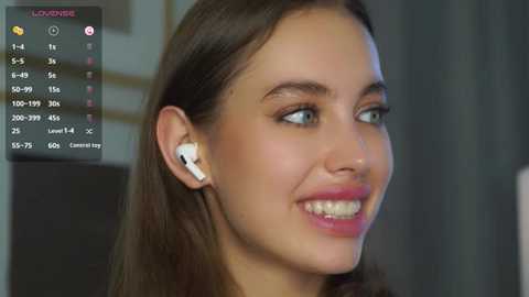 Media: Video of a smiling young woman with straight brown hair, wearing white earbuds, in a dimly lit room, with a digital clock displaying \"9:05\" in the background.