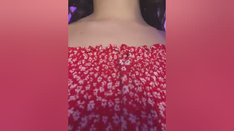 Media: A video of a woman's upper torso, showcasing her bare shoulders and a red, off-the-shoulder dress with white floral patterns. The background is a solid pink gradient.