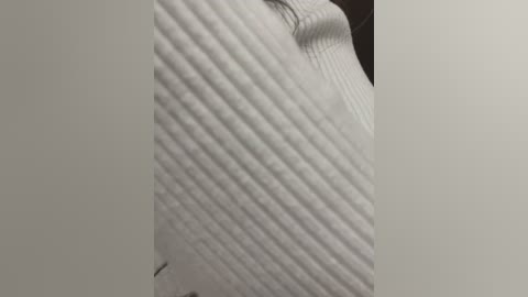 Media: A close-up video of a white, textured sweater with diagonal ribbing, highlighting its soft, slightly wrinkled fabric. The background is plain and dark, emphasizing the sweater's intricate details.