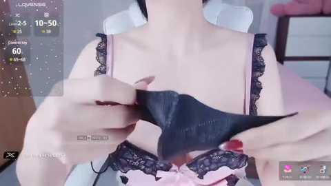 Media: Video of a fair-skinned woman wearing a black lace bra, adjusting the straps. The background shows a white chair and a partially visible wooden shelf.