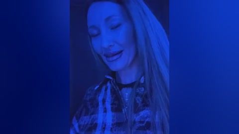 Media: Video of a smiling woman with long blonde hair wearing a plaid shirt, illuminated by a blue light, giving a serene, dreamy ambiance.