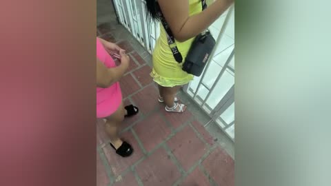 Media: Video of two women in a tiled hallway; one in a bright pink dress, the other in a yellow skirt, with a black bag.