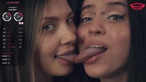 Media: Video of two young women with fair skin, one with a nose piercing, licking each other's lips. Background features a digital screen displaying \"LovemeBig\" and stats.