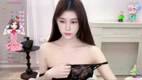 Media: Video of a young Asian woman with long black hair, fair skin, wearing a black lace top, in a room with a white fireplace, colorful toys, and a calendar.