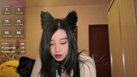 Media: Video of an Asian woman with long black hair and black cat ears, wearing a black leather collar, red lipstick, in a dimly lit room.