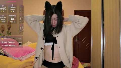 Media: Video of a young woman with long black hair, wearing a white cardigan, black bra, and panties, standing in a bedroom with a bed, wooden door, and social media app screens displaying stats.