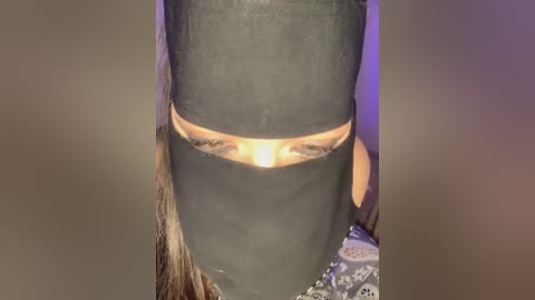 Media: A video showing a person with a black bandana covering their face, revealing only the eyes. The background is blurred with a hint of purple and white.