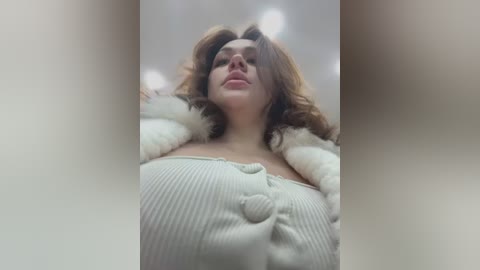 Media: Video of a Caucasian woman with light skin and wavy brown hair, wearing a white off-shoulder sweater with a fur collar, looking up with a neutral expression.