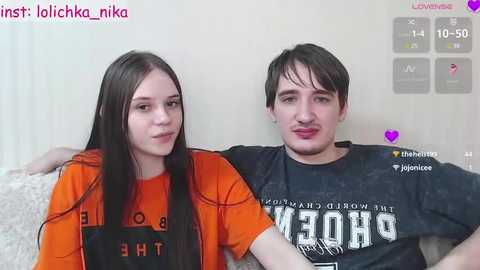 Media: A video of a young couple with long dark hair, wearing orange and black t-shirts, seated on a couch, smiling.