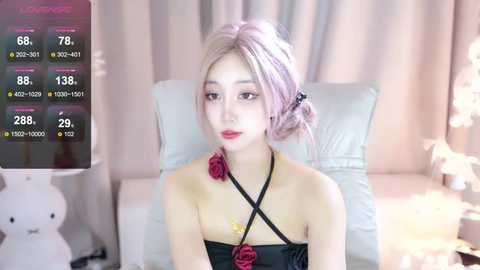 Media: Video of a young East Asian woman with pastel pink hair in a white strapless dress adorned with a red rose, seated on a white couch.