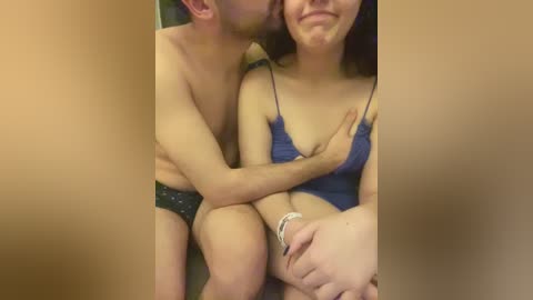 Media: Video of a shirtless man with short hair, kissing a woman with long brown hair and a blue tank top.