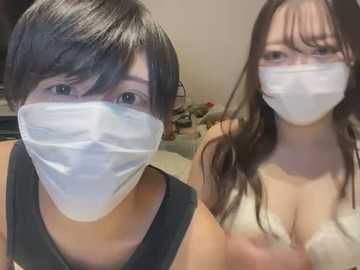 Media: Video of two East Asian women with short black hair, wearing white medical masks and black tank tops, in a dimly lit room with blurred background.