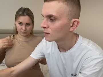 Media: Video of a blonde woman in a beige top adjusting a young man's white shirt collar, both indoors with neutral background.