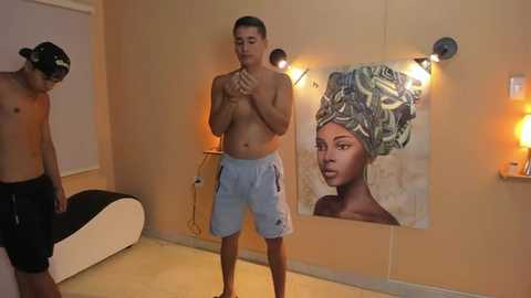 Media: Video of a shirtless man with short hair in light blue shorts, standing in a dimly lit room with a large, colorful portrait of a woman with an African-style headwrap.