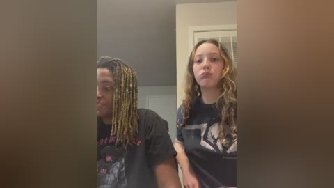 Media: Video of two people: a Black man with dreadlocks in a graphic T-shirt and a Caucasian woman with long, curly hair in a dark T-shirt. They stand indoors, with blurred background.