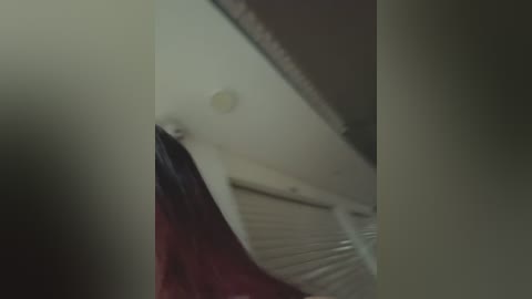 Media: A blurry video showing a ceiling fan with white blades and a beige wall with a light bulb, taken from a low angle.