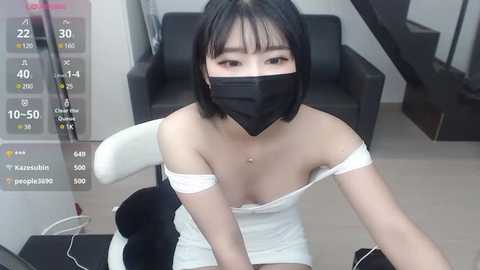 Media: Video of an East Asian woman with short black hair, wearing a white off-shoulder dress, black mask, and gloves, sitting indoors, with a digital interface overlay showing temperature and humidity readings.