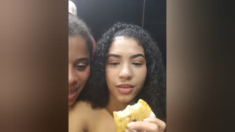 Media: Video of two young women with curly hair, one with braces, smiling, eating a slice of yellow cake, background blurred.