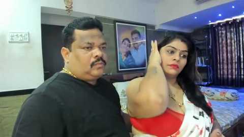 Media: Video of an overweight Indian man and a plus-size woman in a modern bedroom, featuring a bed, wall art, and dark curtains.